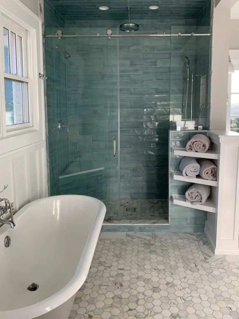 Luxury bathroom with frameless glass shower, blue wall tile, freestanding bathtub, and hexagon tile flooring.