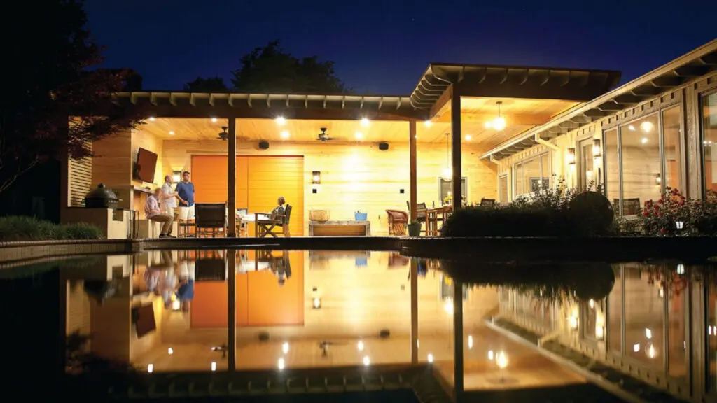 Modern outdoor living space at night with covered patio, pool reflections, and warm architectural lighting