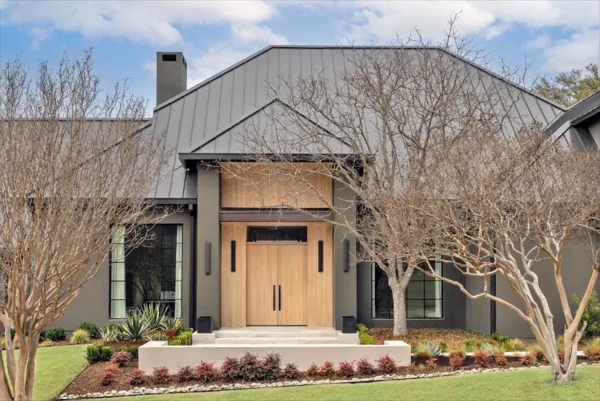Modern custom home exterior with dark metal roof, natural wood front doors, and landscaped front yard