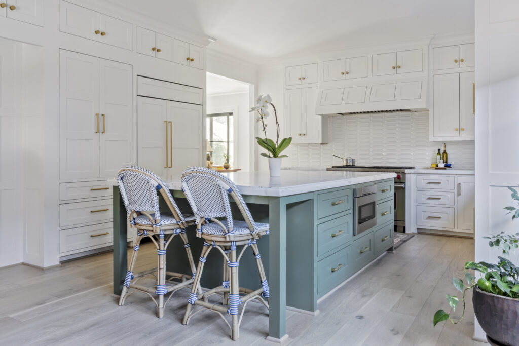 Bright custom kitchen with white cabinetry, blue-gray island, woven bar stools, and brass hardware