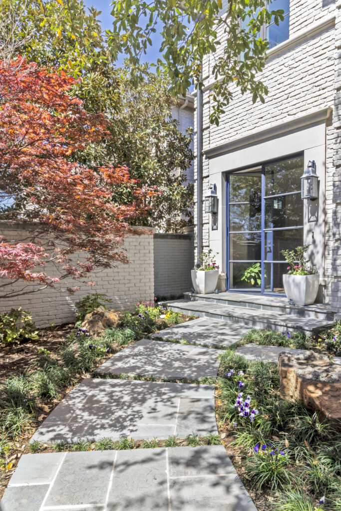 Modern home entrance with stone walkway, landscaped garden, and large steel-framed glass front door