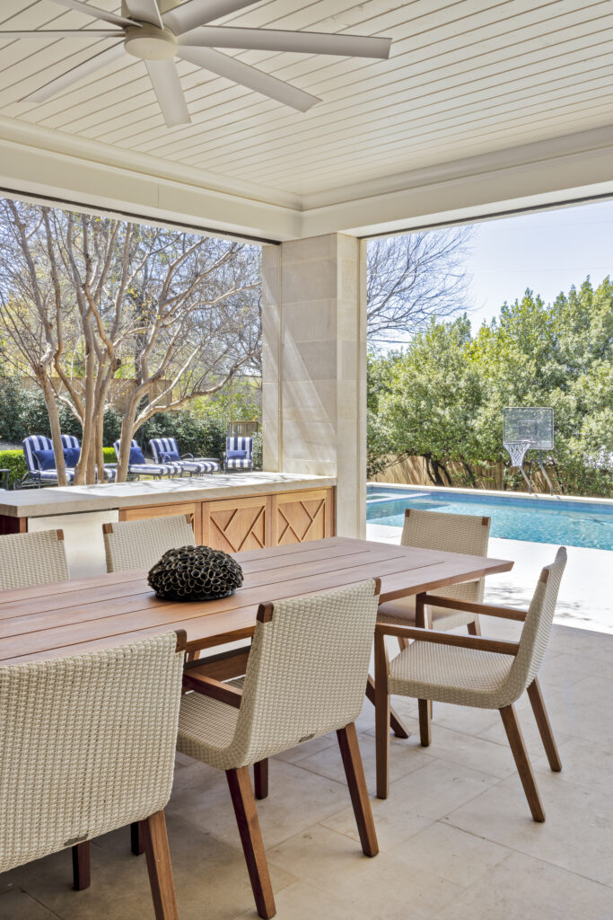Covered outdoor dining area overlooking a backyard pool with lounge seating and trees