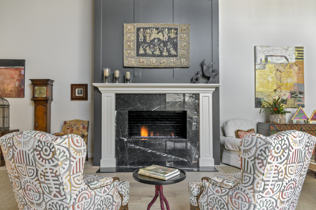 Living room with black marble fireplace, patterned armchairs, eclectic artwork, and modern decor accents