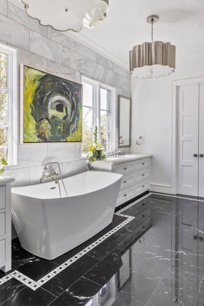 Luxury bathroom with freestanding soaking tub, black marble flooring, white vanity, and modern pendant lighting