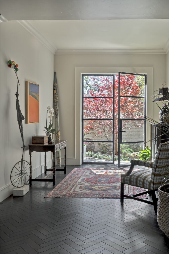 Entry hallway with dark herringbone flooring, vintage decor, patterned rug, and glass door opening to a landscaped courtyard