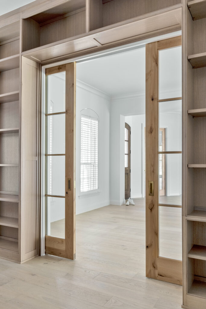 Custom wood sliding doors with built-in shelving and glass panels in a modern interior space