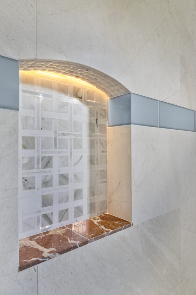 Illuminated shower wall niche with decorative tile inset and blue accent trim in a luxury bathroom