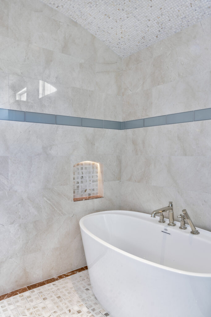 Freestanding soaking tub inside a custom tiled shower with blue accent tile and mosaic ceiling detail