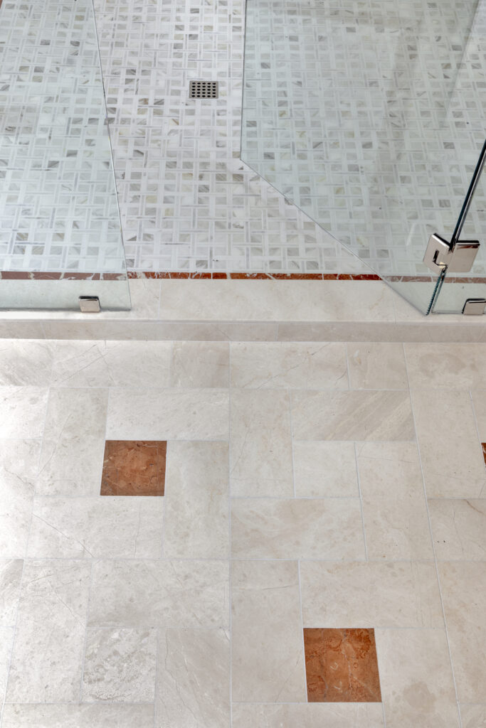 Close-up of luxury bathroom tile flooring and glass shower with decorative stone accents