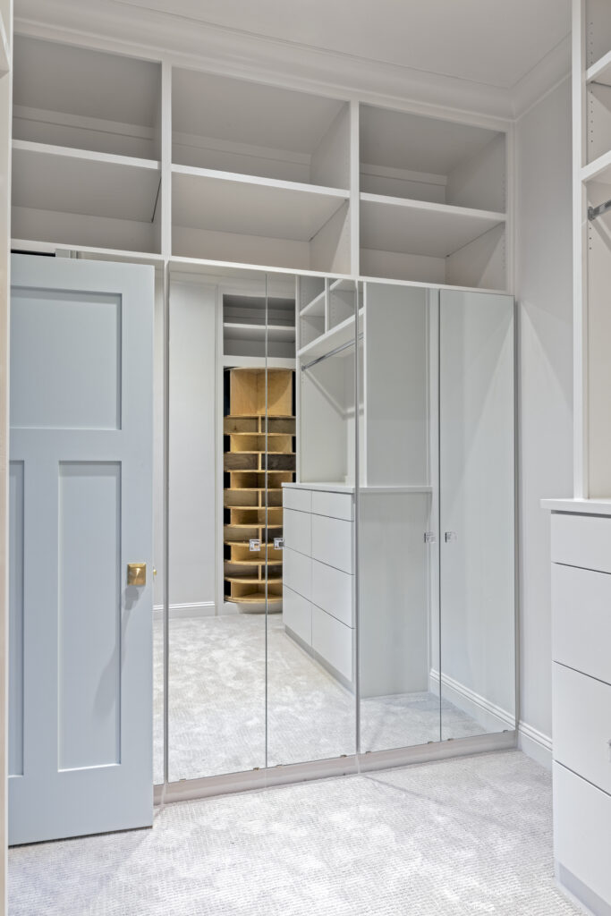 Custom walk-in closet with mirrored doors and built-in shelving in a luxury home