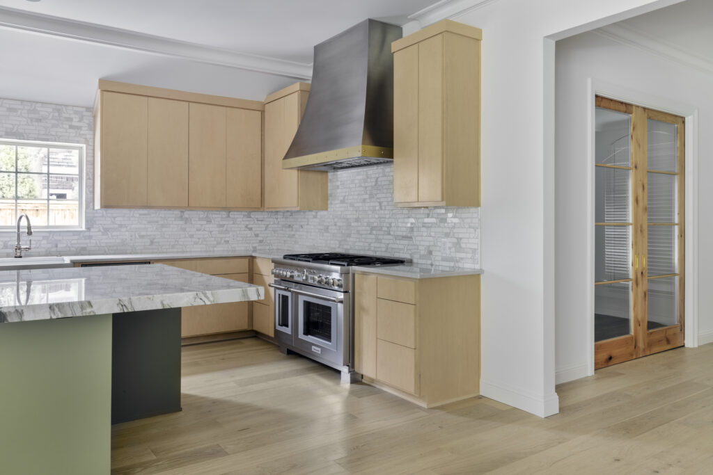 Modern kitchen with light wood cabinetry, marble island countertop, stainless steel range, and custom vent hood