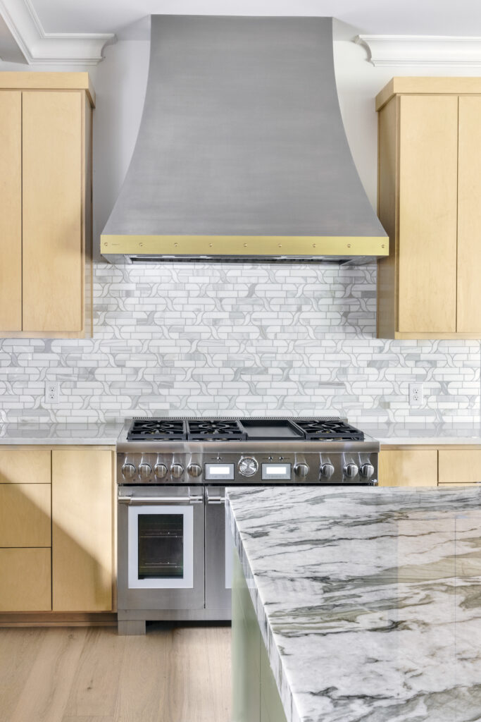Custom kitchen range with oversized vent hood, marble island countertop, and patterned tile backsplash