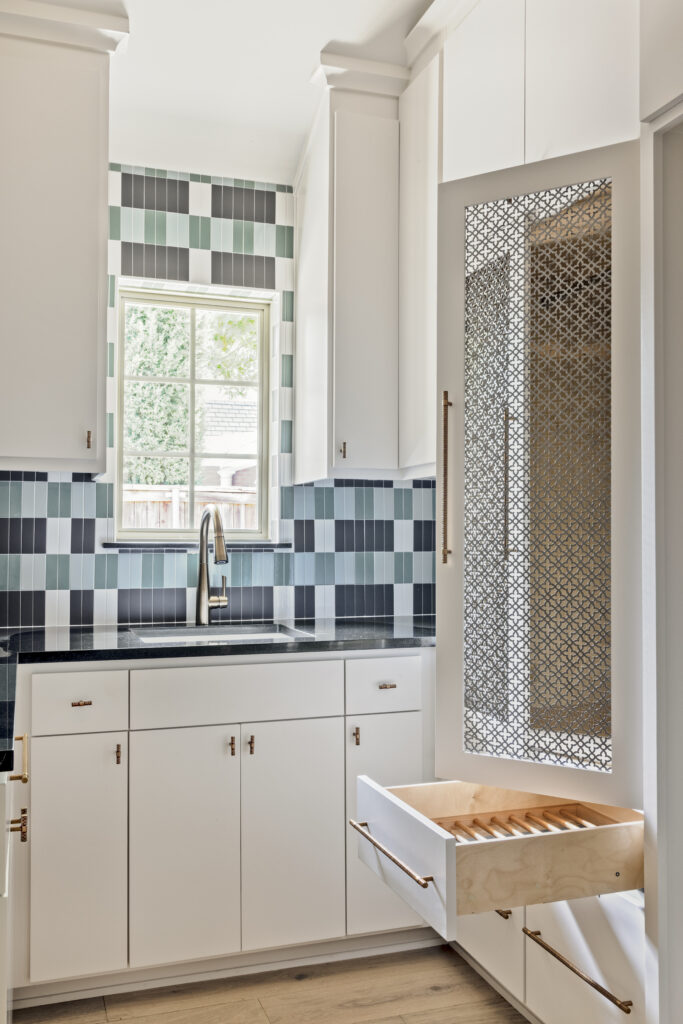 Custom kitchen cabinetry with pull-out storage drawer, decorative metal inserts, and patterned tile backsplash