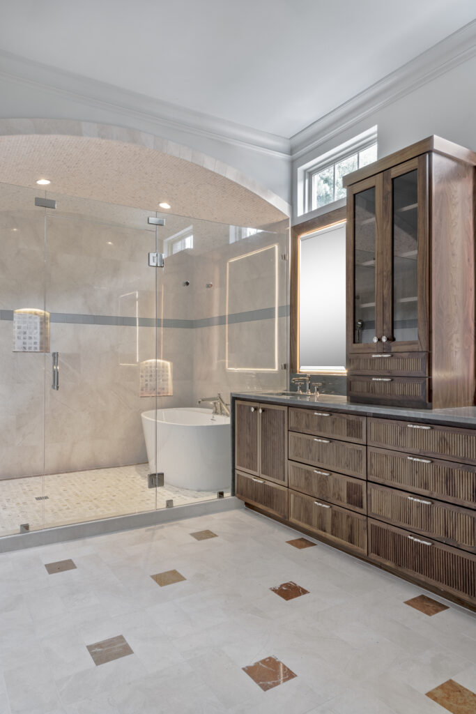 Luxury primary bathroom with custom wood vanity, frameless glass shower, and freestanding soaking tub