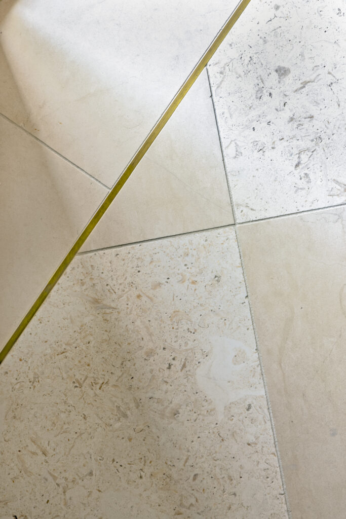 Close-up detail of patterned stone flooring with brass inlay accents in a luxury home