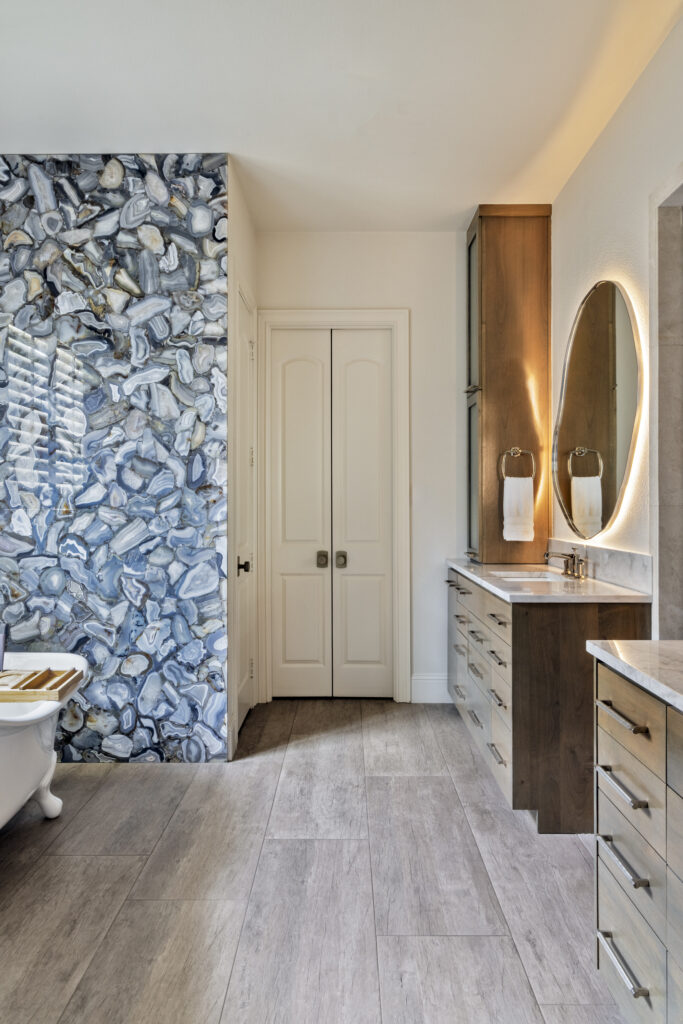 Luxury bathroom with illuminated mirror, wood vanity, and blue stone accent wall