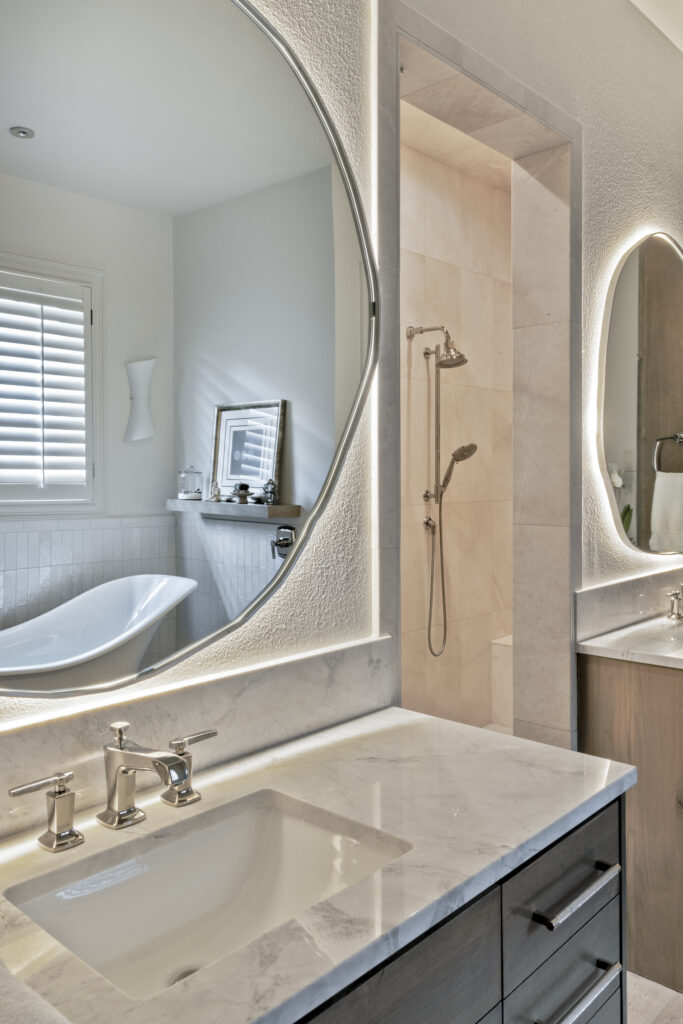 Modern bathroom vanity with illuminated mirror and walk-in shower in a luxury home