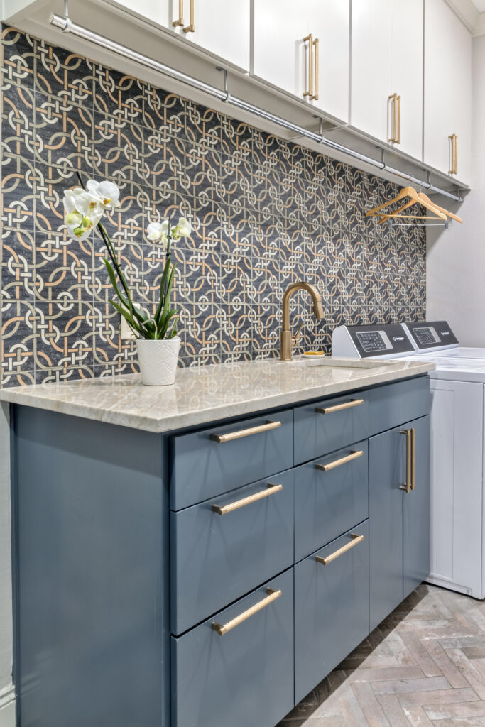 Luxury laundry room with blue cabinetry, patterned wallpaper, and marble countertop